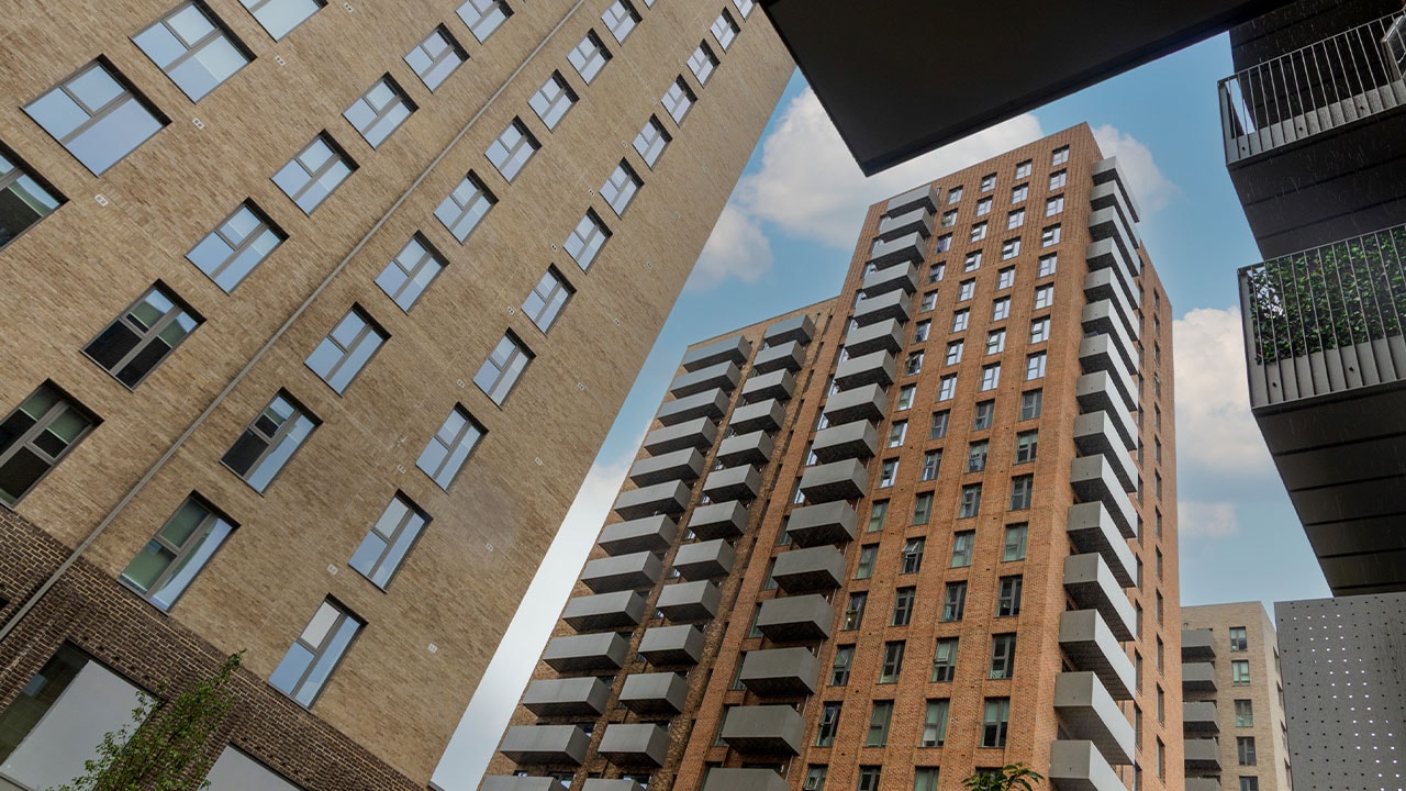 View looking up between residential apartment buildings at One Goodmayes, showing multi-storey brick-built blocks with balconies surrounding a communal courtyard area.